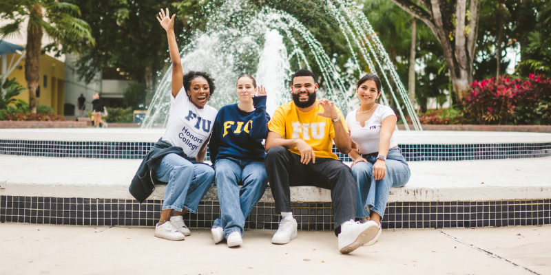 four students posing for the camera in front of a fountain.