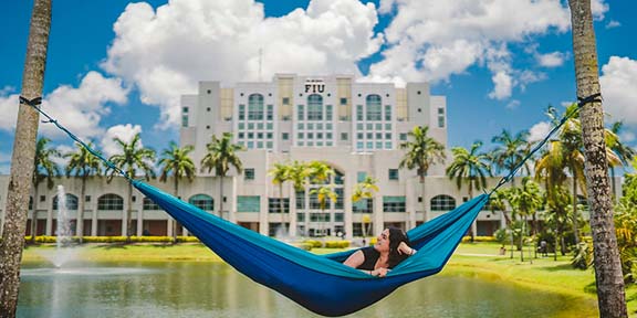 Student laying in a hammock with the backdrop of the lake by Green Library.