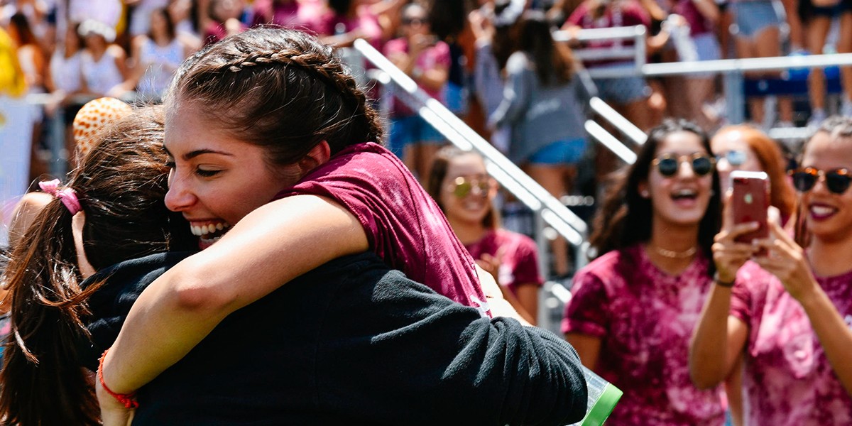 Two students hugging each other at graduation in a warm embrace. 