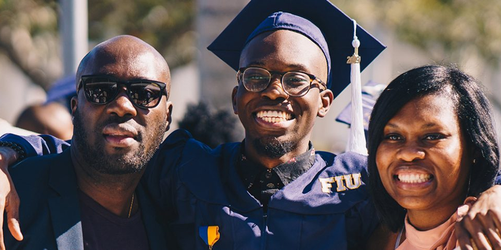 A student who graduated from FIU in his cap and gown posing for pictures with family. 